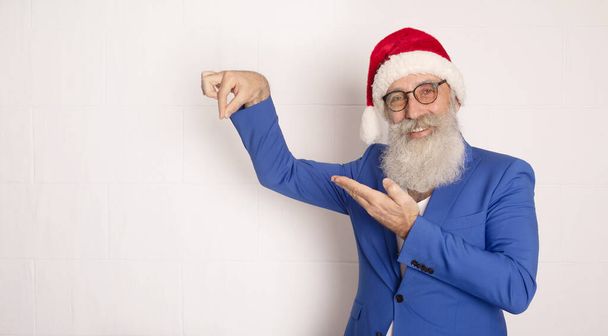 Santa Claus pointing his hand isolated over white. Bearded man in blue suit. Businessman wearing in santa hat. Xmas. New Year. - Foto, Imagen