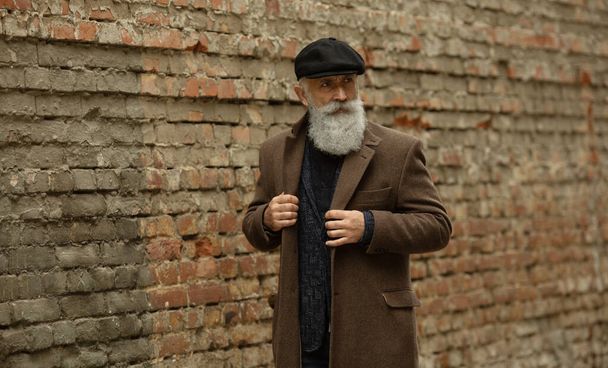 Handsome confident mature man with beard stands in coat on street with copy space for your text message or advertising, fashionable rich male dressed in expensive clothes posing outdoors. - Foto, Bild