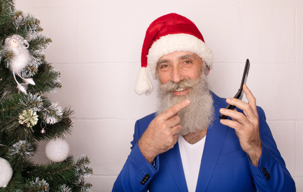Vicces Mikulás piros kalapot visel beszél telefonon, miközben áll fehér háttér. Karácsonykor. Új év. - Fotó, kép
