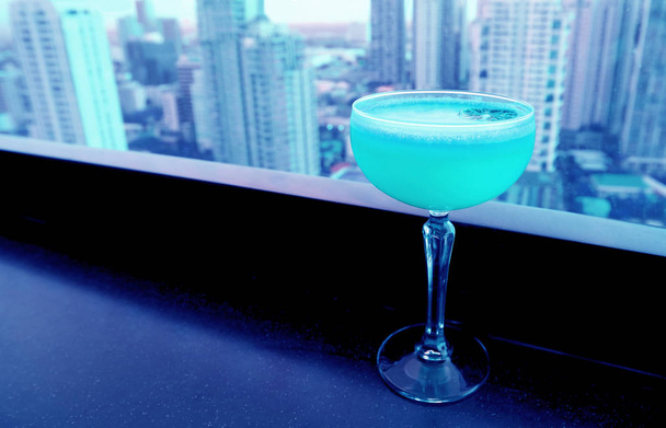 Aqua kék színű koktél a tetőtéri bár asztalán felhőkarcolókkal a háttérben - Fotó, kép