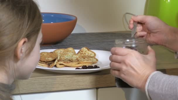 Mutter fügt Sirup zu Pfannkuchen hinzu, während die Familie zu Hause gemeinsam in der Küche frühstückt - Filmmaterial, Video