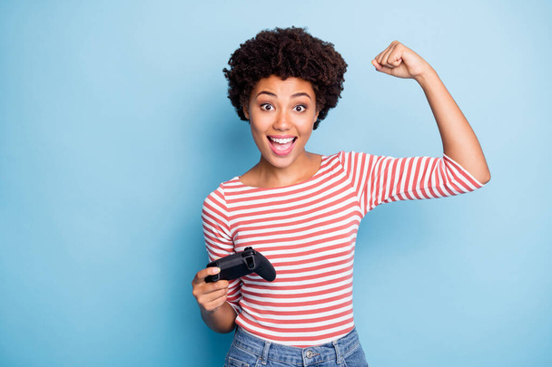 Photo of cheerful positive cute nice pretty student playing with joy stick showing her muscles after having completed another level in jeans denim striped shirt isolated blue pastel color background - Valokuva, kuva