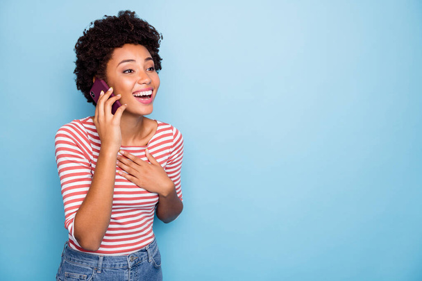 Photo of beautiful crazy dark skin wavy lady hold telephone speaking with best friend listen humorous story wear casual striped sweater jeans isolated blue color background - Foto, afbeelding