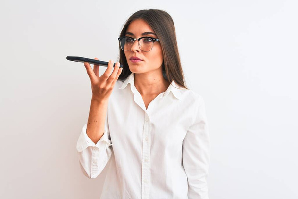 vrouw het dragen van een bril verzenden van bericht op smartphone over geïsoleerde witte achtergrond met een zelfverzekerde uitdrukking op slimme gezicht denken serieus - Foto, afbeelding