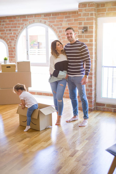 Mooie familie met een kind staande in nieuw huis rond kartonnen dozen - Foto, afbeelding