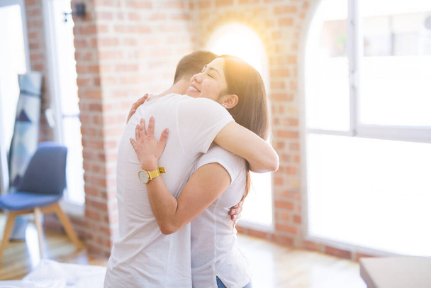 Young beautiful couple hugging at new home around cardboard boxes - Foto, imagen