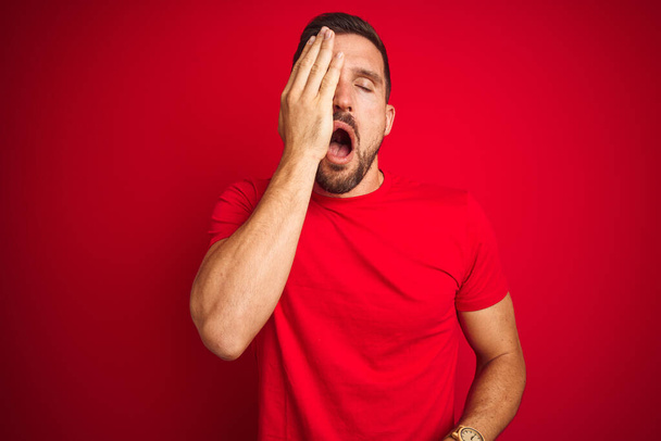 junger gutaussehender Mann in lässigem T-Shirt über rotem isoliertem Hintergrund gähnt müde und verdeckt mit der Hand das halbe Gesicht, Augen und Mund. Gesicht schmerzt vor Schmerzen. - Foto, Bild