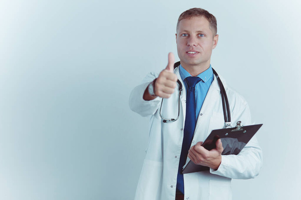 Portrait of handsome doctor in white coat holding a folder, showing Ok sign - Foto, afbeelding