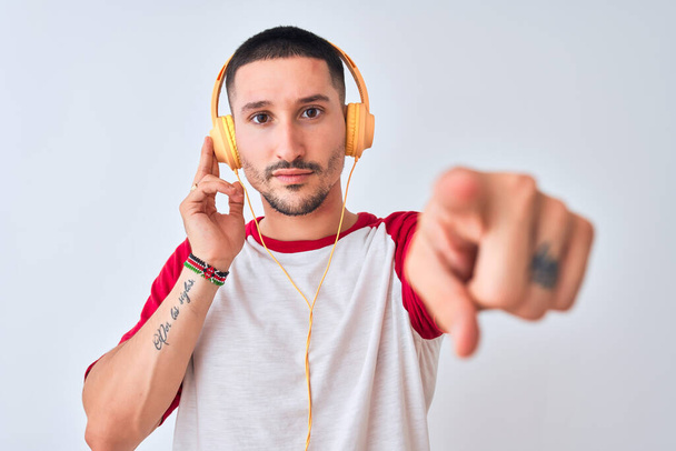 Young handsome man wearing headphones over isolated background pointing with finger to the camera and to you, hand sign, positive and confident gesture from the front - Foto, Bild