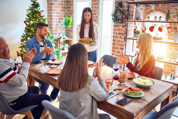 Mooie familie bijeenkomst glimlachend gelukkig en vol vertrouwen. Persoon staande met geroosterde kalkoen die thuis Kerstmis viert - Foto, afbeelding
