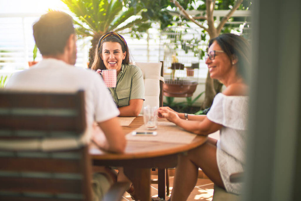 Kaunis perhe istuu terassilla juomassa kahvia puhumassa ja hymyilemässä
 - Valokuva, kuva