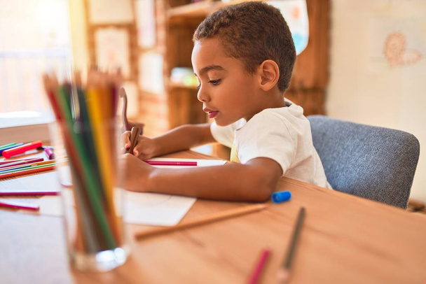 Красивий афроамериканський малюк сидить малювати автомобільну іграшку, використовуючи маркерну ручку на столі в дитячому саду
 - Фото, зображення