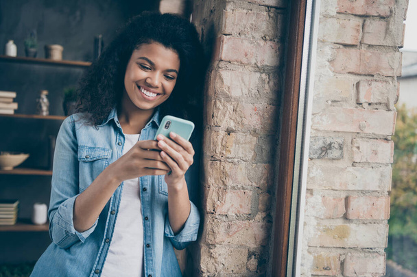 Closeup photo of amazing dark skin curly lady holding telephone reading boyfriend sms leaning brick window wall wear casual denim outfit modern flat indoors - Foto, immagini