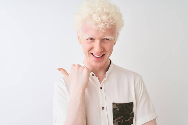 Jeune homme blond albinos portant chemise décontractée debout sur fond blanc isolé pointant et montrant avec le pouce sur le côté avec sourire heureux visage
 - Photo, image
