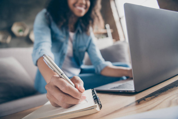 Cropped blurry focus photo of amazing dark skin curly lady browsing notebook writing pen plan list diary sitting cozy sofa wear casual denim outfit flat indoors - Foto, Imagem