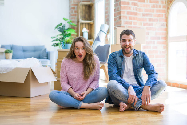 Young beautiful couple moving to a new house sitting on the floor afraid and shocked with surprise expression, fear and excited face. - Foto, Imagem
