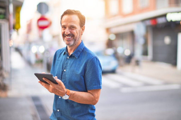 Μεσήλικας όμορφος επιχειρηματίας που χρησιμοποιεί tablet χαμογελώντας στο δρόμο - Φωτογραφία, εικόνα