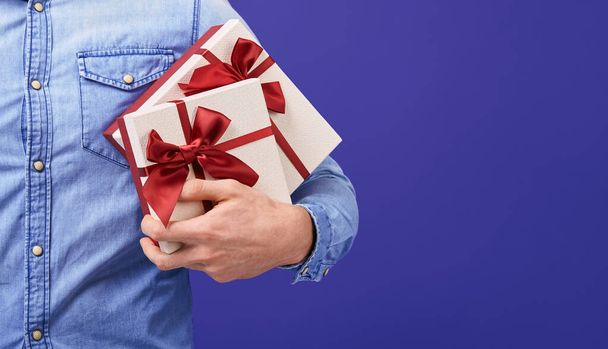 Man in a blue denim shirt with two gifts with a red cap in his hands - Foto, immagini