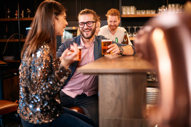 Un piccolo gruppo di amici seduti nel pub irlandese al bancone del bar, bevono birra e chiacchierano. Vita notturna
. - Foto, immagini