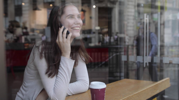 Młoda kobieta w kawiarni pije kawę i używa smartfona - Beautiful br - Materiał filmowy, wideo