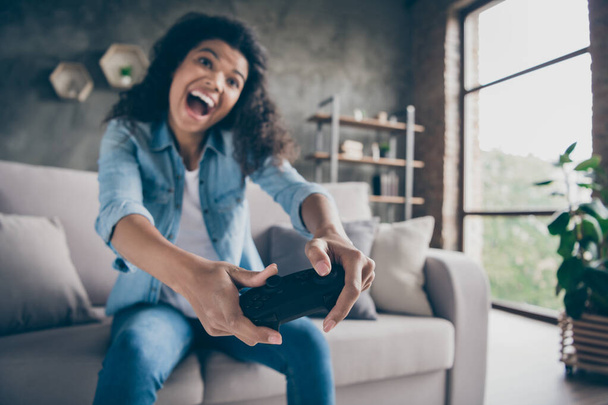 Blurry focus photo of funny pretty dark skin wavy lady hold gamepad console joystick addicted gamer excited sitting cozy couch casual denim outfit living room indoors - Фото, зображення
