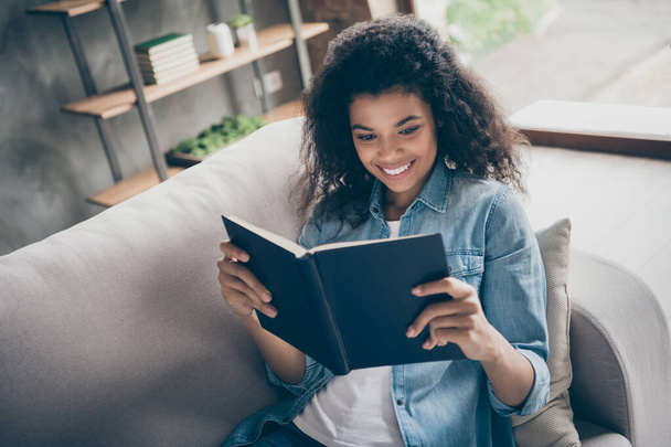 Closeup photo of pretty dark skin wavy lady hold book reading favorite love story historic novel homework lying comfy couch casual denim outfit living room indoors - Foto, afbeelding