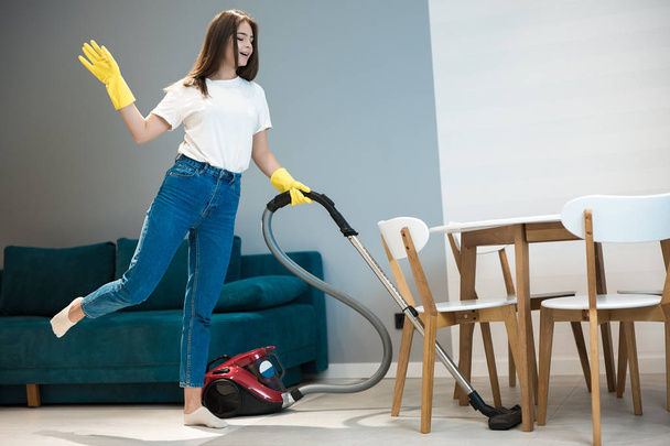 cute young woman in yellow gloves dancing while doing vacuum cleaning in the living room - Fotoğraf, Görsel
