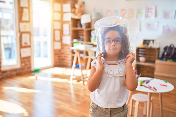 Schönes Kleinkind mit Brille, Einhorn-Diadem und Plastikwürfel auf dem Kopf spielt als Astronaut im Kindergarten - Foto, Bild
