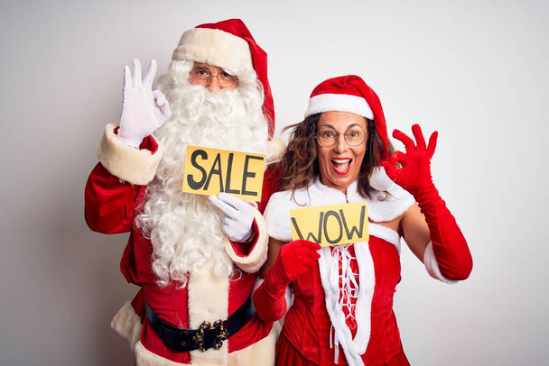 Pari yllään Santa puku tilalla wow ja myynti banneri yli eristetty valkoinen tausta hymyillen positiivinen tekee ok merkki käsin ja sormin. Onnistunut ilmaisu
. - Valokuva, kuva