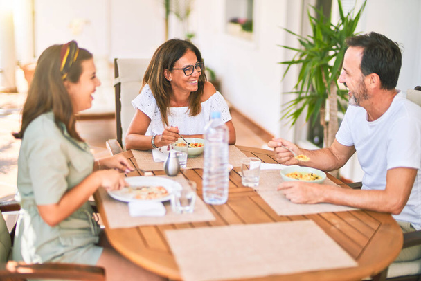 Hermosa familia sentada en la terraza comiendo alimentos hablando y sonriendo
 - Foto, imagen