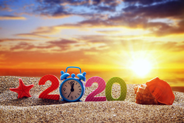 Number 2020, alarm clock and sea shell on the sand beach. Happy New Year and  summer holiday concept. - 写真・画像