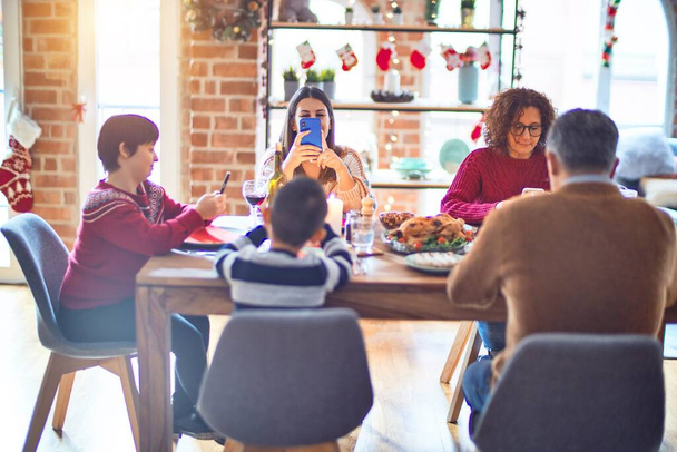 Hermosa familia sonriendo feliz y confiada. Comer pavo asado usando un smartphone celebrando la Navidad en casa
 - Foto, imagen