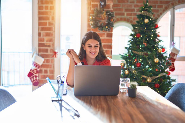 美しい女性が一緒に手でクリスマスツリーの周りの自宅でノートパソコンで作業テーブルに座って、リラックスして陽気な笑顔の指を越えました。成功と楽観的 - 写真・画像