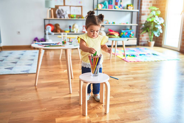 Piękny maluch stojący trzymając kolorowe ołówki w przedszkolu - Zdjęcie, obraz