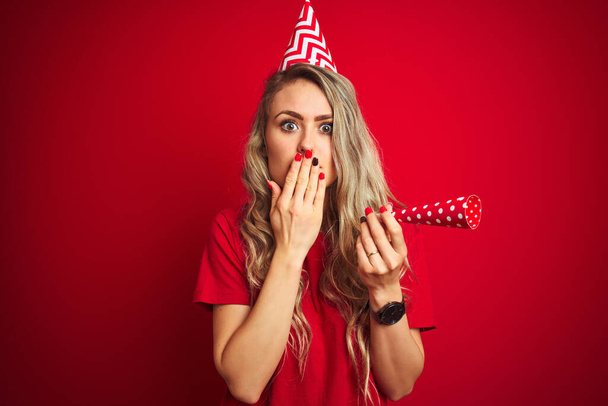 Mladá krásná žena na narozeninové oslavy přes červené izolované pozadí kryt ústa s rukou šokované hanbou za omyl, vyjádření strachu, strach v tichu, tajný koncept - Fotografie, Obrázek