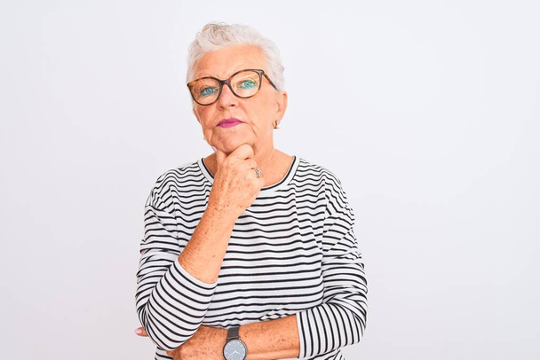 Senior grey-haired woman wearing striped navy t-shirt glasses over isolated white background looking confident at the camera with smile with crossed arms and hand raised on chin. Thinking positive. - Фото, зображення