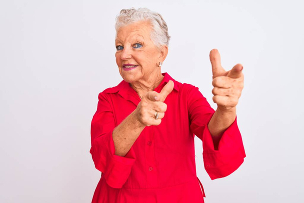 Starší šedovlasá žena v červené neformální košili, stojící nad izolovaným bílým pozadím a ukazující prstem na kameru se šťastnou a zábavnou tváří. Dobrá energie a vibrace. - Fotografie, Obrázek