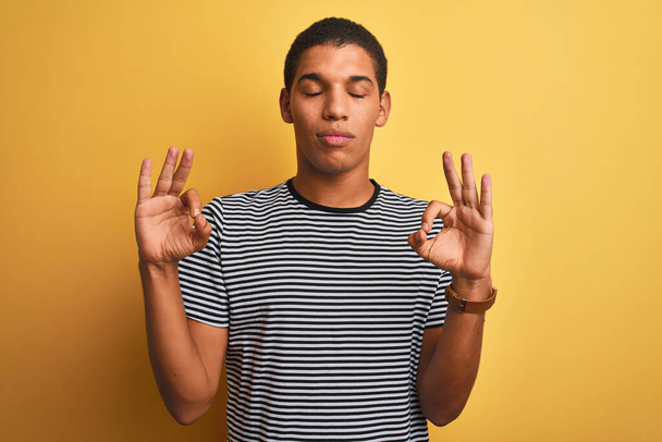 Young handsome arab man wearing navy striped t-shirt over isolated yellow background relax and smiling with eyes closed doing meditation gesture with fingers. Yoga concept. - Фото, зображення
