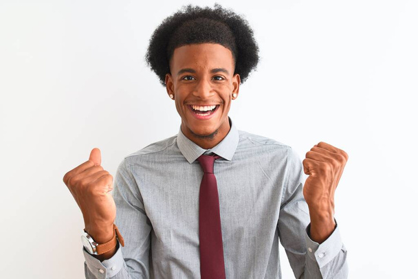 Joven hombre de negocios afroamericano con corbata de pie sobre un fondo blanco aislado celebrando sorprendido y sorprendido por el éxito con los brazos levantados y los ojos abiertos. Concepto ganador
. - Foto, imagen