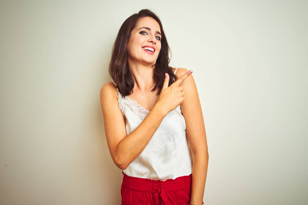 Νεαρή όμορφη γυναίκα φορώντας t-shirt στέκεται πάνω από λευκό απομονωμένο φόντο χαρούμενα με ένα χαμόγελο του προσώπου που δείχνει με το χέρι και το δάχτυλο μέχρι το πλάι με ευτυχισμένη και φυσική έκφραση στο πρόσωπο - Φωτογραφία, εικόνα