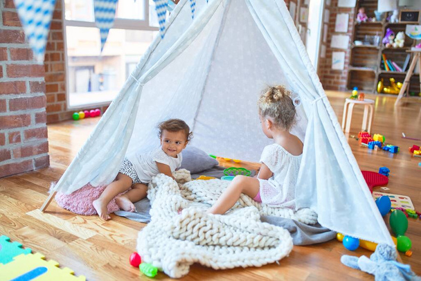Beaux tout-petits jouant à l'intérieur tipi sur couverture autour de beaucoup de jouets à la maternelle
 - Photo, image