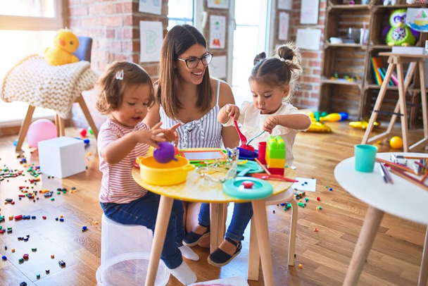 Fiatal gyönyörű tanár és kisgyermekek játszanak étkezés segítségével műanyag étel és evőeszköz játék az óvodában - Fotó, kép