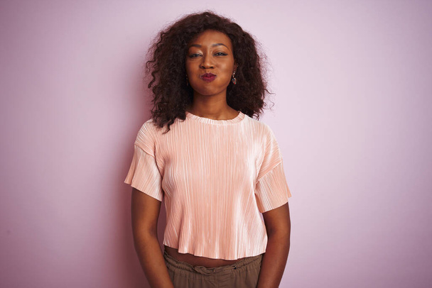 Nuori afrikkalainen amerikkalainen nainen t-paidassa seisoo yli eristetty vaaleanpunainen tausta turvotusta posket hauska kasvot. Suu täynnä ilmaa, hullu ilme
. - Valokuva, kuva