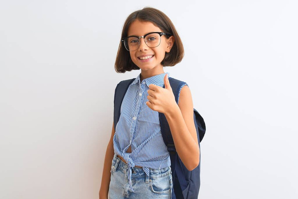 Krásná studentka dívka nosí batoh a brýle na izolovaném bílém pozadí dělá šťastné palce nahoru gestem ruky. Schválení výrazu při pohledu na fotoaparát s úspěchem. - Fotografie, Obrázek
