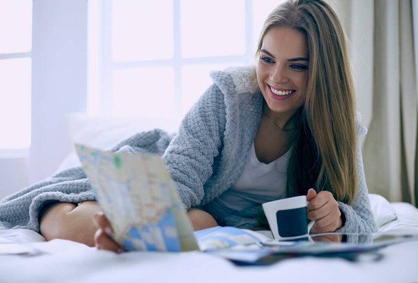 Relaxed young woman sitting on bed with a cup of coffee and digital tablet - Foto, Bild
