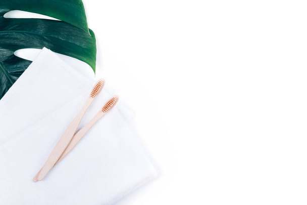 Дві бамбукові зубні щітки на рушниках ізольовані на білому тлі та тропічному листі монастиря. Концепція без пластику
. - Фото, зображення