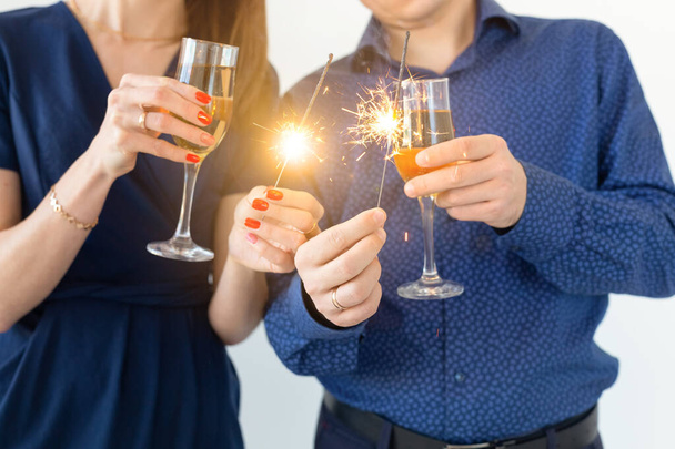 Nahaufnahme von Mann und Frau, die Weihnachten oder Silvesterparty mit Bengalischen Lichtern und Champagnergläsern feiern. - Foto, Bild