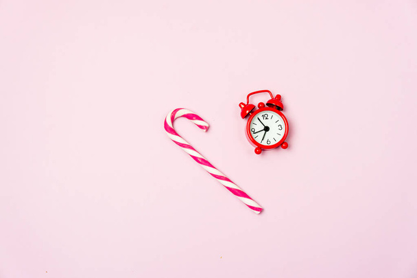Small Red Clock and Christmas Candy Cane on Pink Background Food Christmas Morning Concept Top View Flat Lay - Фото, зображення