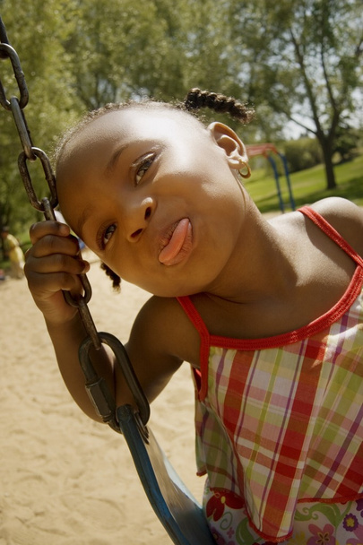 Young Girl Sticking Out Her Tongue While On The Swing Set At The Park - Fotografie, Obrázek