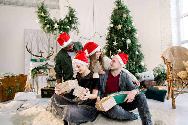 Cheerful young four international people celebrate Christmas and New Year together in cozy decorated studio. - Φωτογραφία, εικόνα